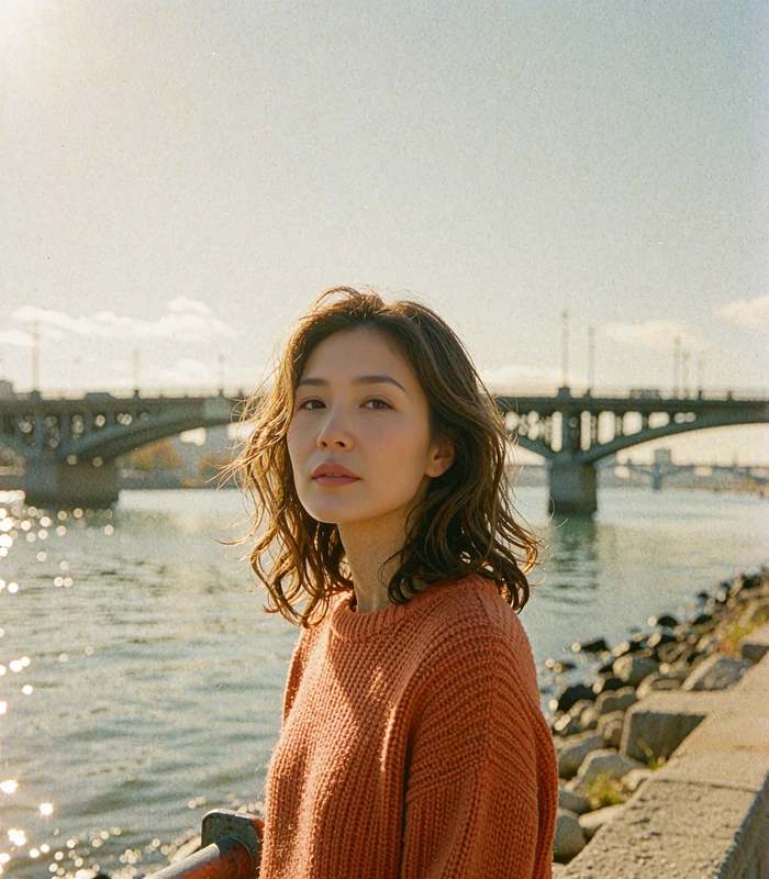 Korean-heritage woman in a burnt-orange sweater on a riverside walkway